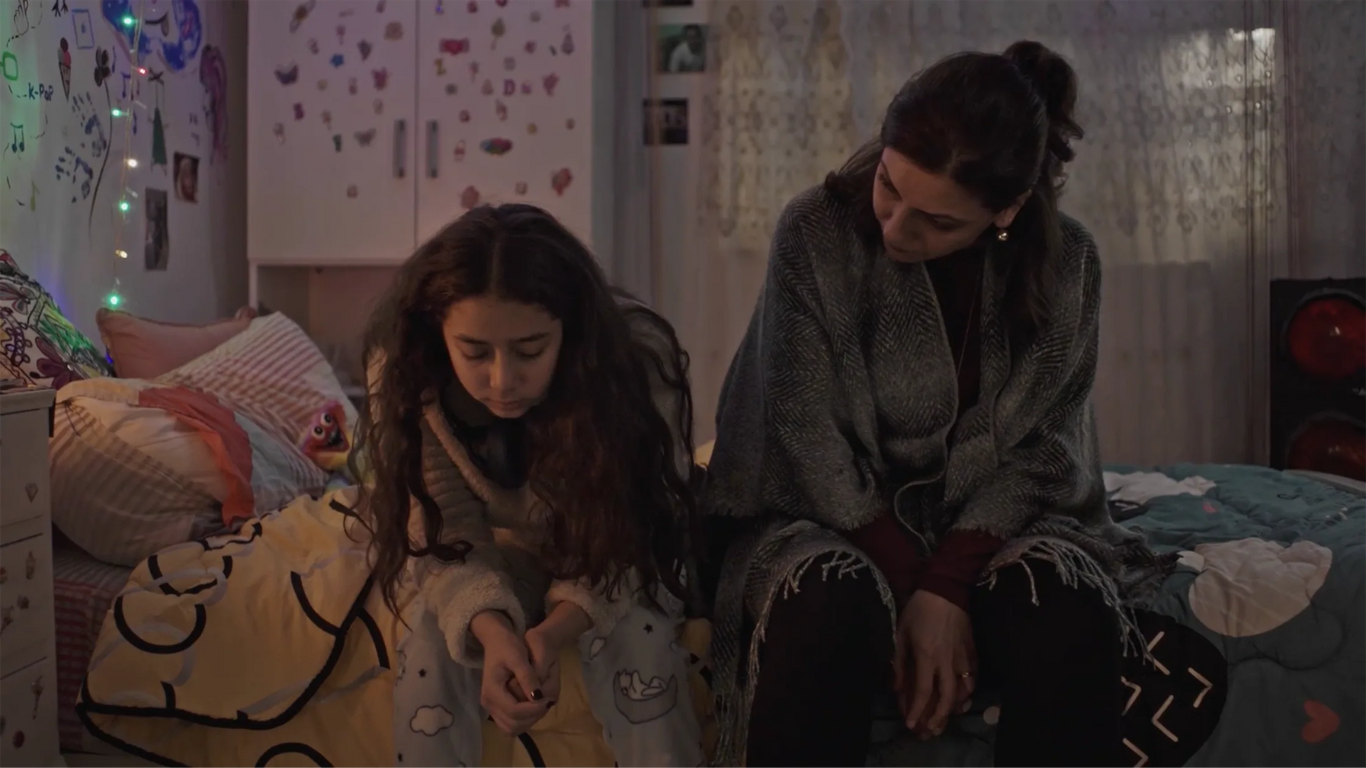 Young girl sat looking sad on her bed with a woman comforting her